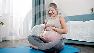 Portrait of beautiful pregnant woman stroking her big belly after practicing yoga and fitness on mat at home. Concept of