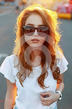 Portrait of a beautiful pretty young redhead hipster woman in trendy sunglasses in a stylish white t-shirt
