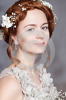Portrait of beautiful red-haired bride. She has a perfect pale skin with delicate blush. White flowers in her hair.