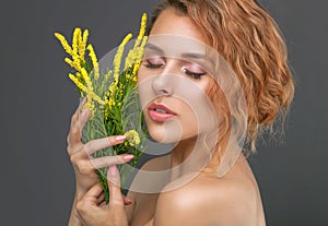 Portrait of a beautiful red-haired curly woman with fresh nude make-up, thick eyebrows and with clean skin,she holds yellow