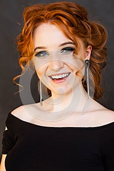 Portrait of a beautiful red-haired girl with long earrings. Girl smiling and posing on a black background