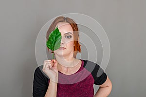 Portrait of a beautiful red-haired woman, half of her face closed by a large green leaf of a Chinese rose. Women`s health, natura