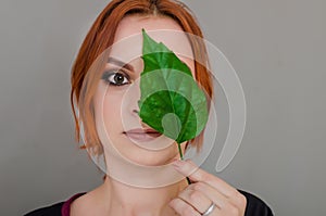 Portrait of a beautiful red-haired woman, half of her face closed by a large green leaf of a Chinese rose. Women`s health, natura