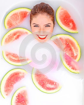 Portrait of a beautiful red-haired woman takes a bath with milk and slices of watermelon. Spa treatment for skin