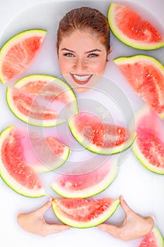 Portrait of a beautiful red-haired woman takes a bath with milk and slices of watermelon. Spa treatment for skin