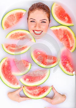 Portrait of a beautiful red-haired woman takes a bath with milk and slices of watermelon. Spa treatment for skin