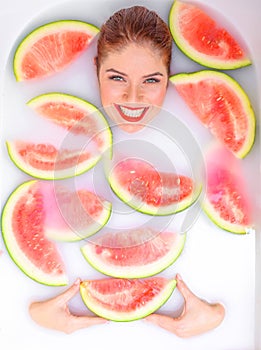 Portrait of a beautiful red-haired woman takes a bath with milk and slices of watermelon. Spa treatment for skin