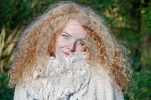 Portrait of a beautiful reddish blond woman in her forties with wild curls stands in the green forest, copy space