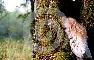 Portrait of a beautiful redhead woman in her forties with wild red curls and a fur scarf collar stands in a willow tree, partially