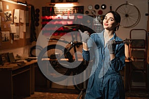 Portrait of a beautiful repairwoman in workwear at the bicycle workshop pointing with finger on space for text