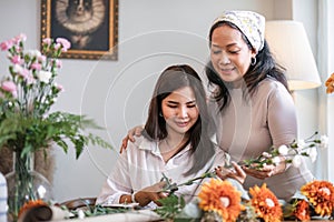 Portrait of a beautiful retired Asian woman focuses on arranging a vase with fresh flowers in a workshop. Lifestyle