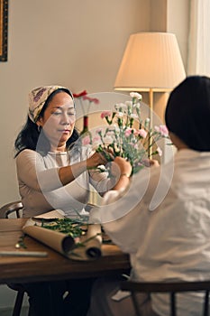 Retired Asian woman focuses on arranging a vase with fresh flowers in a workshop