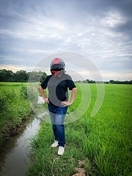 Portrait of beautiful rider woman in yellow green motorcycle helmet and colorful light summer dress in jungle on tropical field