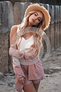 Portrait of a beautiful, romantic and stylish female model with long loose blonde hair in a straw hat. Countryside landscape, natu