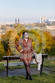 Portrait of beautiful romantic young woman sitting on bench in park, autumn in Prague, yellow brown golden leaves, cute stylish