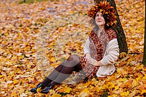 Portrait of beautiful romantic young woman with wreath of autumn brown golden and red maple leaves, cute stylish girl in dress