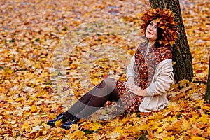 Portrait of beautiful romantic young woman with wreath of autumn brown golden and red maple leaves, cute stylish girl in dress