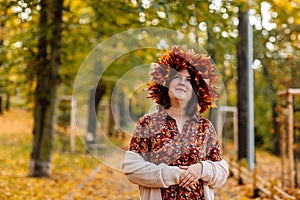 Portrait of beautiful romantic young woman with wreath of autumn yellow brown golden and red maple leaves, cute stylish girl in