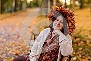 Portrait of beautiful romantic young woman with wreath of autumn yellow brown golden and red maple leaves, cute stylish girl