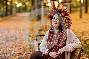 Portrait of beautiful romantic young woman with wreath of autumn yellow brown golden and red maple leaves, cute stylish girl