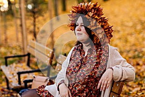 Portrait of beautiful romantic young woman with wreath of autumn yellow brown golden and red maple leaves, cute stylish girl