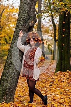 Portrait of beautiful romantic young woman with wreath of autumn yellow brown golden and red maple leaves, cute stylish girl in