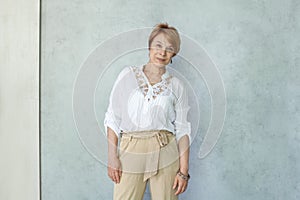 Portrait of beautiful senior woman in casual white blouse standing on gray background