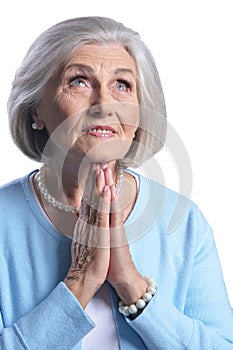 Portrait of beautiful senior woman in light blue blouse praying