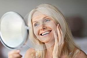 Portrait of beautiful senior woman looking in miror and touching face, checking her wrinkles, admiring her beauty
