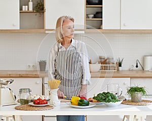 Portrait of beautiful senior woman standing in kitchen and looking aside while preparing healthy food