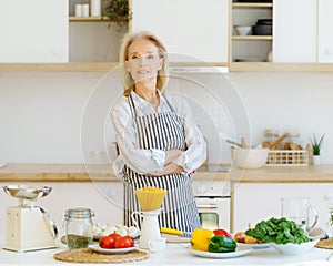 Portrait of beautiful senior woman standing in kitchen and smiling at camera while preparing healthy food