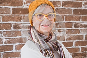 Portrait of beautiful senior woman wearing winter cap and scarf - brick wall background