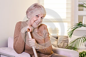 Portrait of beautiful senior woman with white hair and walking stick. Portrait of senior woman sitting on sofa at home. Smiling