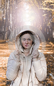 Portrait of beautiful sensitive woman in jacket with a hood standing on the road of park at the autumn day