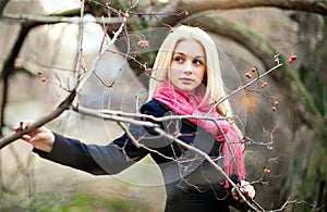 Portrait of beautiful sensual girl with thick blond hair, looking to the side, in a black coat and pink scarf fall among the trees