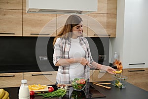 Portrait of a beautiful serene happy pregnant woman, housewife holding a kitchen knife and preparing food in the kitchen island,