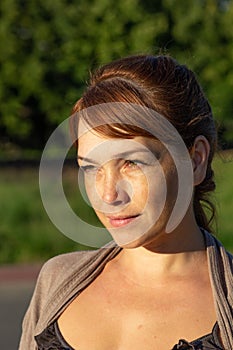 Portrait of beautiful serious middle-aged woman with calm face looking aside in summer green park