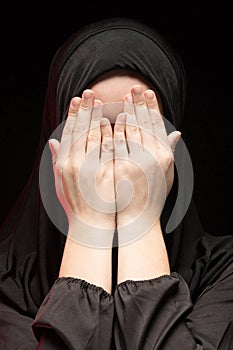 Portrait of beautiful serious young muslim woman wearing black hijab with hands near her face as praying concept on