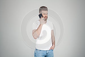 Portrait of beautiful sexy bearded man. he stands in the profile and talks over the phone. he stands in front of the white