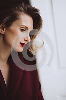 Portrait of a beautiful sexy girl with curls and bright full lips with red lipstick in a burgundy coat. Beauty and fashion. Soft