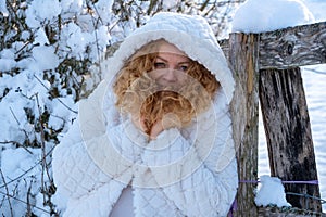 Portrait of beautiful sexy mature redhead woman, with red curly hair in white hooded coat in winter nature sun backlight