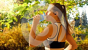 Portrait of beautiful sexy woman with ponytail drinking water from bottle while running and jogging in autumn park