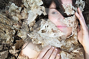 Portrait of beautiful sexy young woman with dark brown hair and blue eyes, with white holed maple autumn leaves, forest bathing,