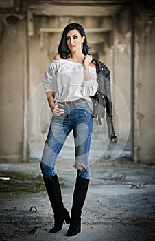 Portrait of beautiful young woman with modern outfit, leather jacket, jeans, white blouse and black boots