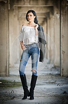 Portrait of beautiful young woman with modern outfit, leather jacket, jeans, white blouse and black boots