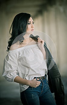 Portrait of beautiful young woman with modern outfit, leather jacket, jeans, white blouse and black boots