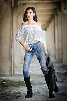 Portrait of beautiful young woman with modern outfit, leather jacket, jeans, white blouse and black boots