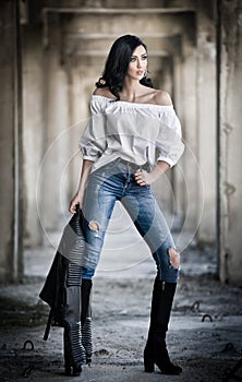 Portrait of beautiful young woman with modern outfit, leather jacket, jeans, white blouse and black boots
