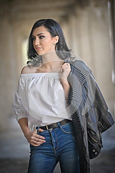 Portrait of beautiful young woman with modern outfit, leather jacket, jeans, white blouse and black boots