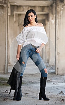 Portrait of beautiful young woman with modern outfit, leather jacket, jeans, white blouse and black boots